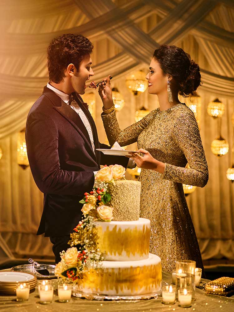 wedding cake, couple with cake, bride, groom, bridal outfit, groom outfit, black tuxedo, golden gown, bridal hairstyle ideas, hair bun,